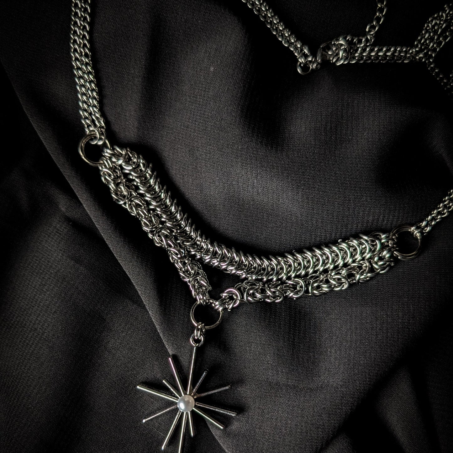 Silver chain necklace with a star-shaped pendant on a black fabric background