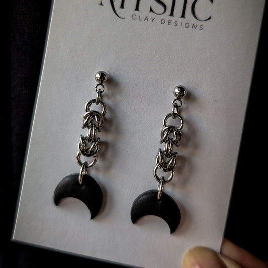 Black crescent moon earrings with chains on a Mystic Clay Designs card.