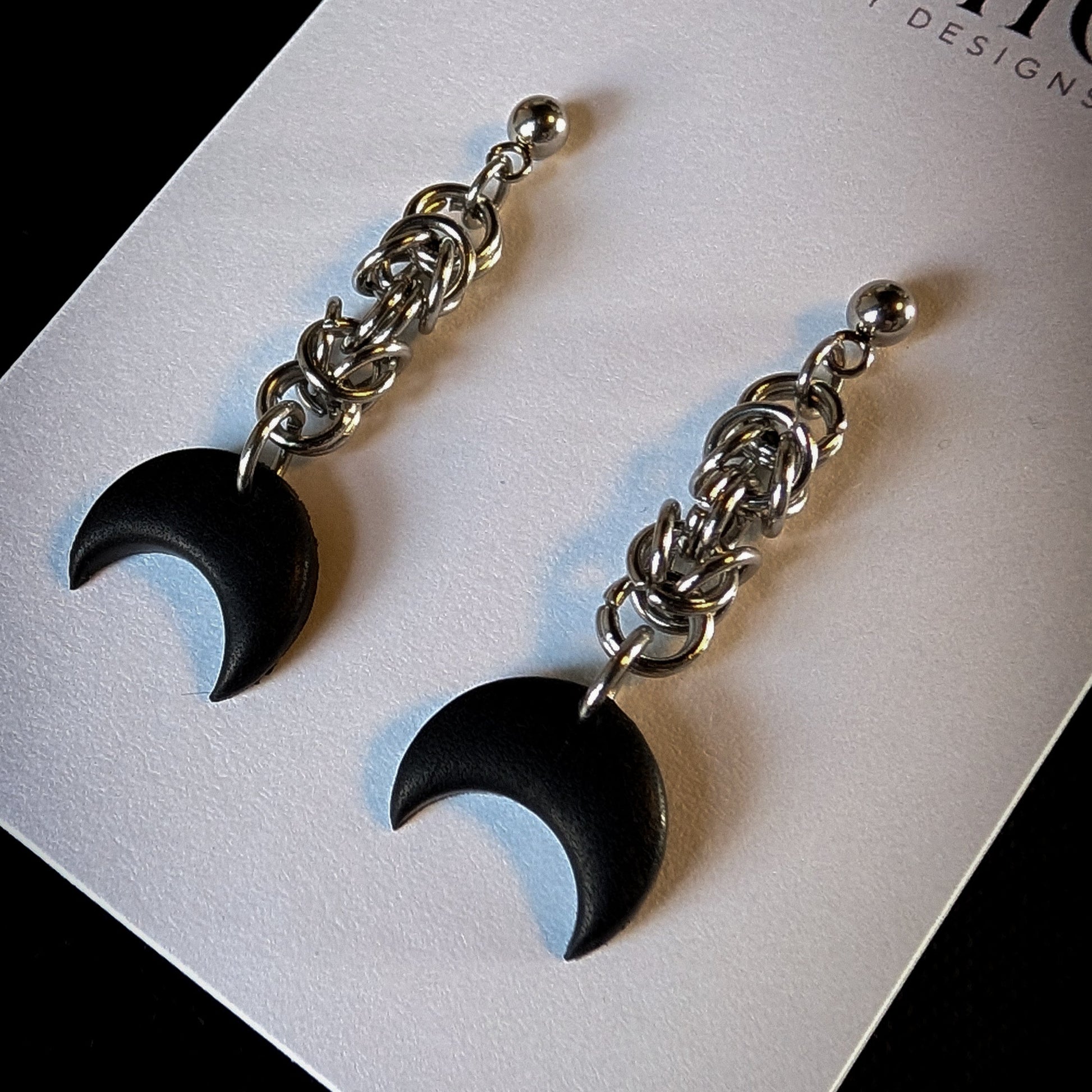 Black crescent moon earrings with silver chains on a card with 'Mystic Clay Designs' branding.