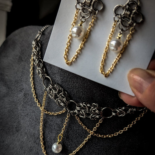 Gold and silver chain necklaces with pearl accents on a dark surface.
