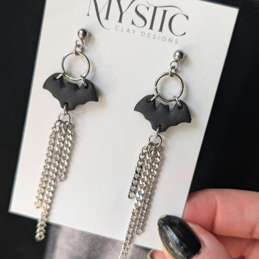 Bat-shaped earrings on a Mystic brand card held by a hand.