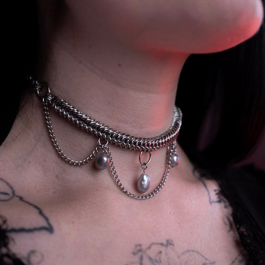 Close-up of a person wearing a silver chain necklace with freshwater pearls, visible tattoos on the neck and shoulders.