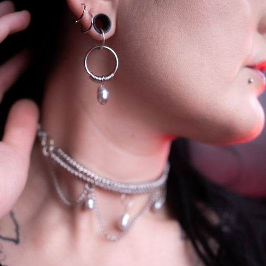 Close-up of a person wearing silver hoop earrings and necklaces with a blurred background