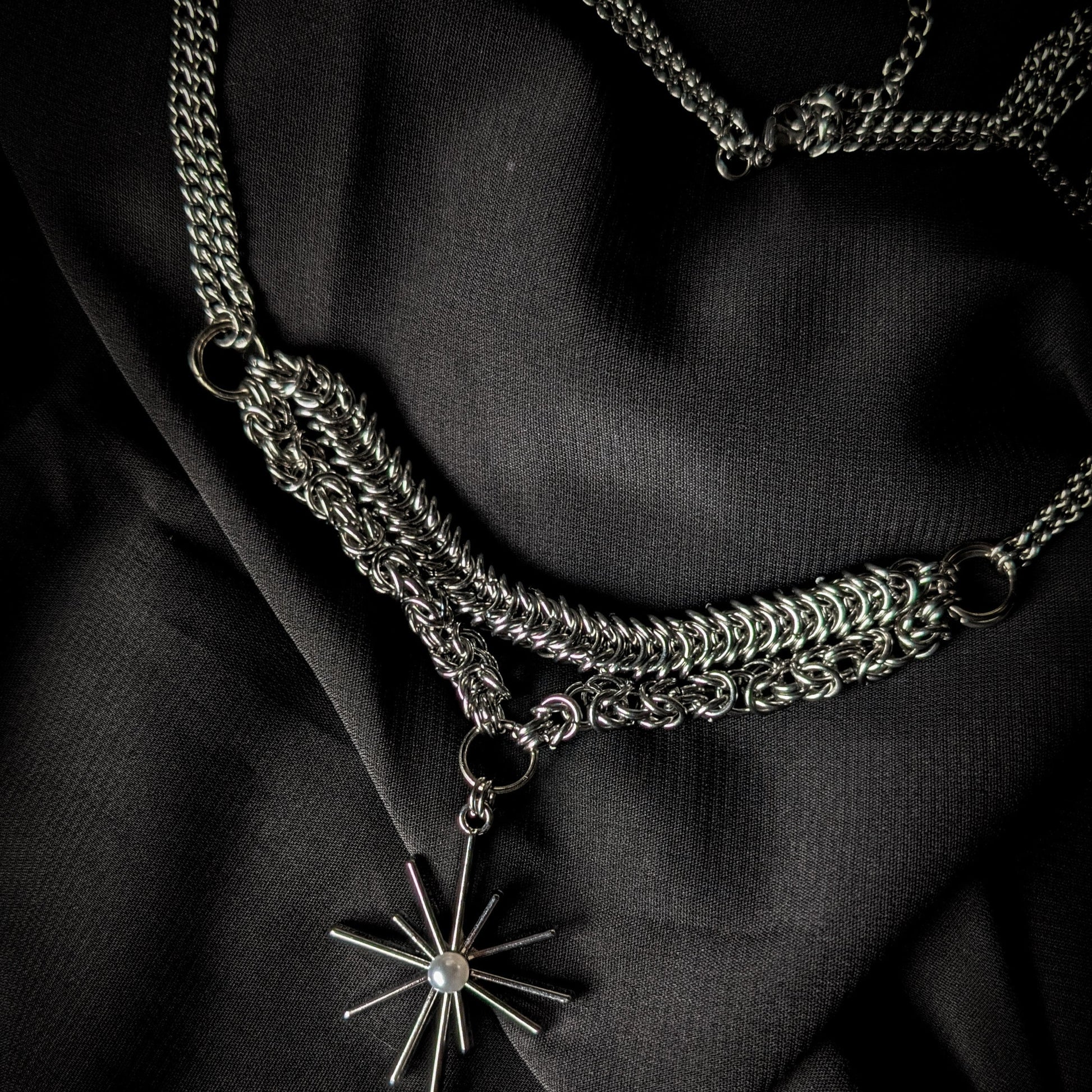 Silver chain necklace with a star-shaped pendant on a black fabric background