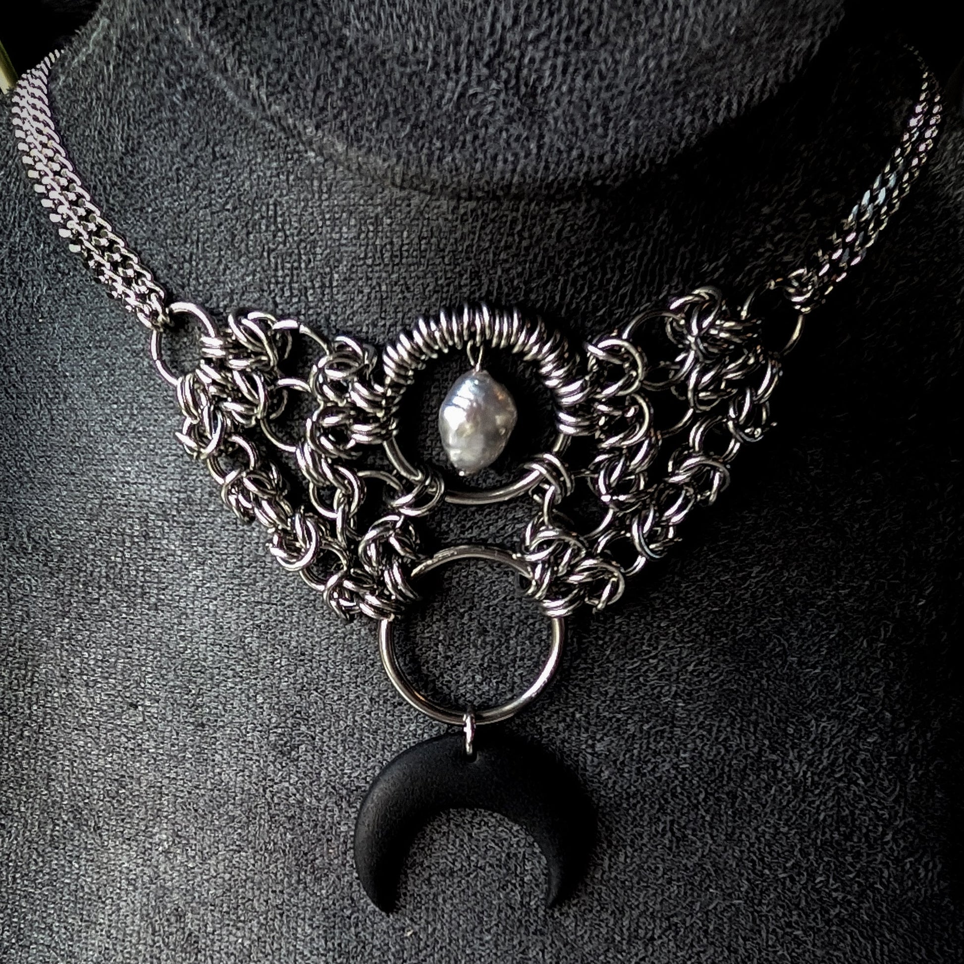 Stainless steel chainmaille necklace with a crescent moon pendant on a dark background